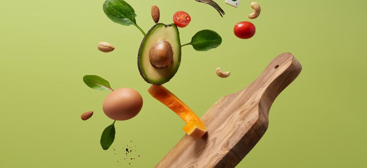 A creative arrangement of paleo diet ingredients floating above a wooden board on a green background.