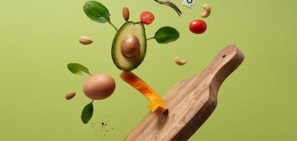 A creative arrangement of paleo diet ingredients floating above a wooden board on a green background.