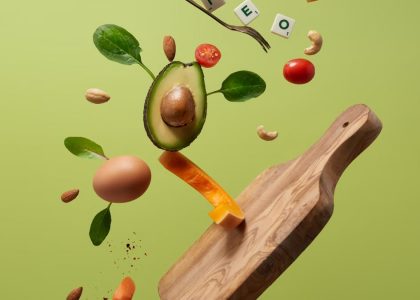 A creative arrangement of paleo diet ingredients floating above a wooden board on a green background.